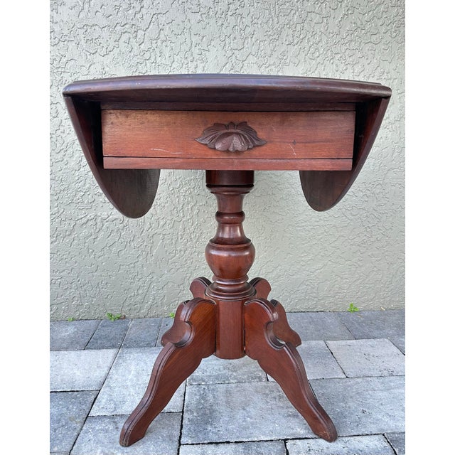 Antique oval shaped drop leaf table. It has 2 leafs with wood brackets that hold them up when raised, a single ornate...