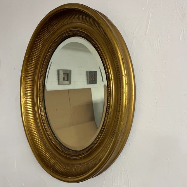 Vintage antique Hollywood Regency oval mirror painted gold. Mirror is beveled. Has some mild flecks in the mirror you...
