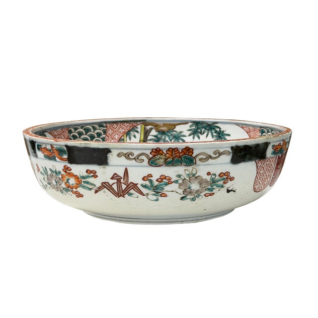 This finely crafted porcelain bowl features a shallow, rounded profile with a gently flared rim and a distinct circular...