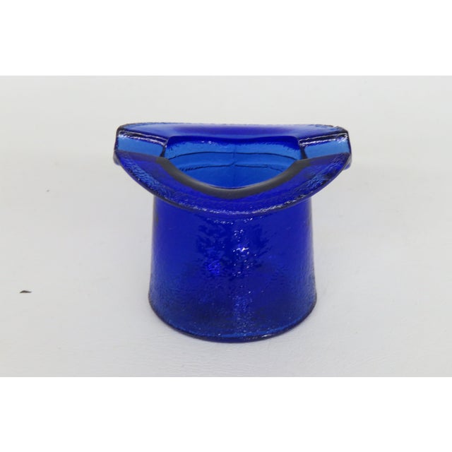 This lovely small ash tray is made of glass. This charming ashtray is in the shape of an upside-down top hat, with two...