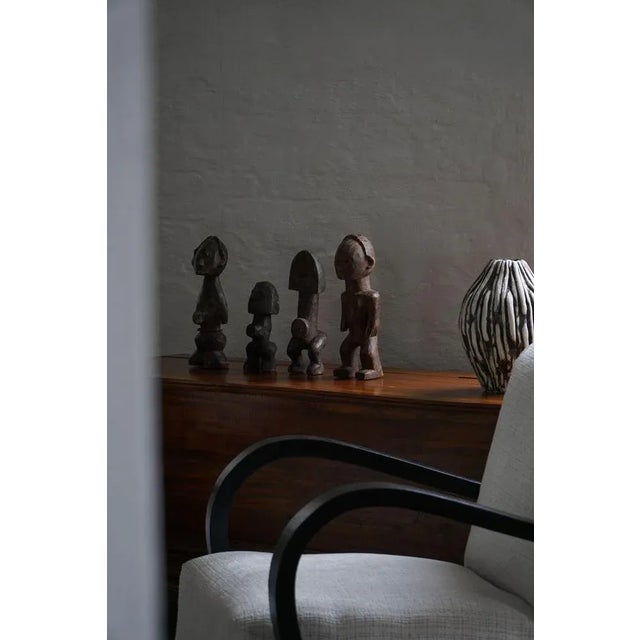 A collection of four hand-carved wooden sculptures from West Africa, each piece unique in its form and expression. Crafted...