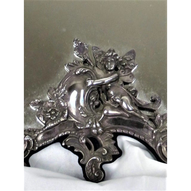 A vintage sterling silver easel stand mirror. Ornate repose cherubs, flowers and scrolls. Back cover with fabric blue...