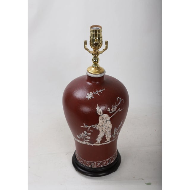 This vintage vase lamp is hand-painted with pictures of chinoiseries characters and flowers on a red background and is...