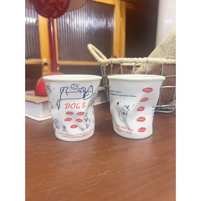 A pair of creative pleated ceramic cups; designed to mimic the look of disposable paper cups, they feature a unique,...