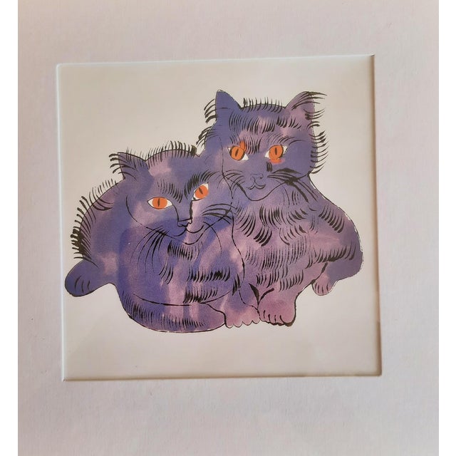 Andy Warhol's print titled "Two Cats" features two playful purple cats with striking red eyes, created around 1995. This...