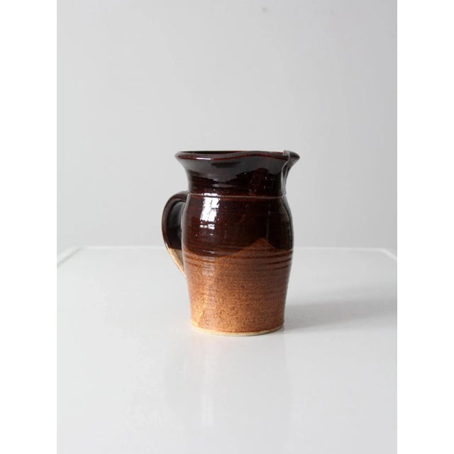 This hand-crafted studio pottery pitcher by Brian Marx features a rich two-tone glaze in deep chocolate and tawny brown....