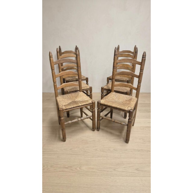 A charming set of six vintage wooden dining chairs featuring distinctive ladder-back backrests, turned uprights, and...