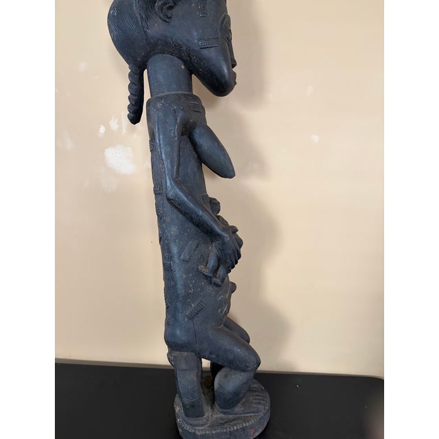 Baule female maternity figure sitting on a stool and holding a baby from the 20th century. This is made of wood and black...