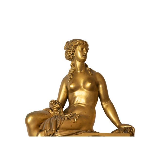 This French Empire mantel clock features a seated female figure, finely sculpted, draped in flowing fabric, and positioned...