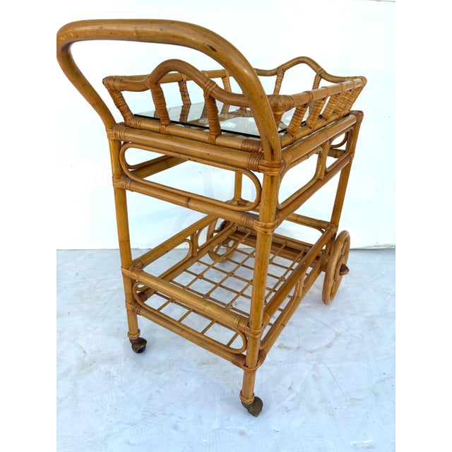 A two-tier bamboo bar cart with a removable tray. The front feet are made of wood, and the back feet are brass casters.