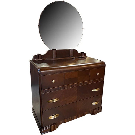 Vintage Art Deco waterfall vanity dresser featuring a rounded top, large circular mirror, and warm wood finish. The...