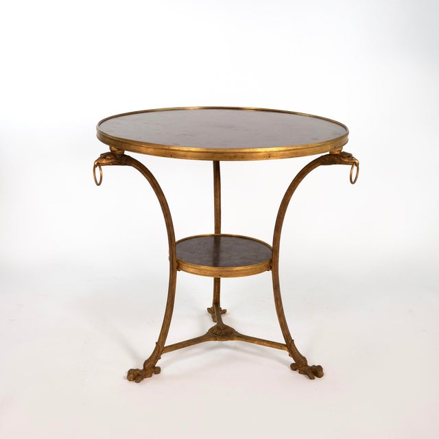 A gilt-bronze gueridon with a circular black fossil marble top set within a molded bronze rim and a conforming lower tier...