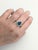 A blue zircon glows in a brilliant electric blue at the centre of this solid 14K white gold ring, encircled by thirty-four...