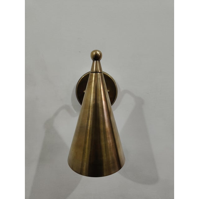 Beautiful handcrafted antique brass cone wall sconce featuring a clean and elegant mid-century inspired silhouette. The...