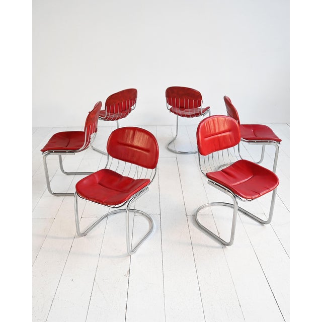Set of six chromed tubular steel chairs, with space-age lines, featuring original carmine red faux leather cushions....
