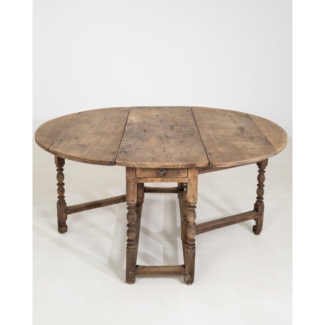 This drop-leaf gateleg table makes its impression through dark walnut, oval top. The piece dates to 19th Century, sourced...