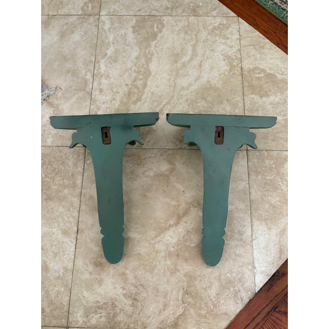 This pair of beautifully carved and fluted wall brackets are painted in an antiqued patina of soft teal green with gilded...