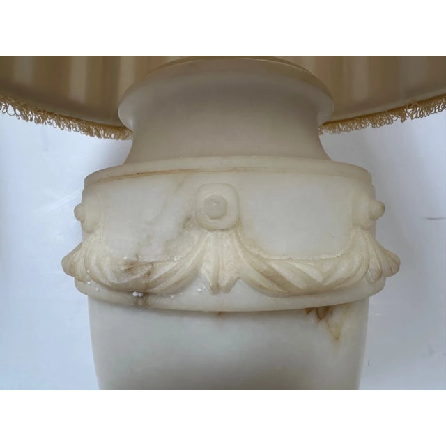 Elegant sculptural pair of urn shaped alabaster table lamps having pretty wreath decoration around the periphery and silk...