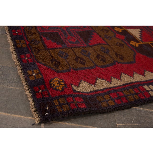 A Mid-20th century hand knotted vintage balouch wool rug with a red field and multi-color accents on a vintage design....