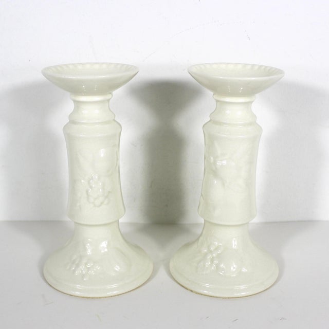 Pair of creamy white porcelain candleholders. These have a beaded rim and raised fruit detail. They hold a standard taper...
