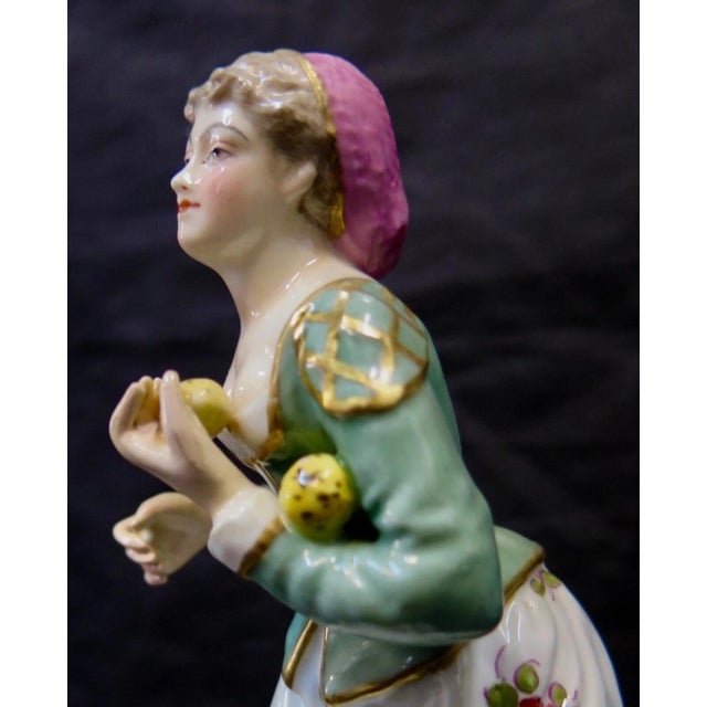 This vintage late 19th century hand painted Meissen porcelain figurine identifies a German woman carrying yellow fruit....
