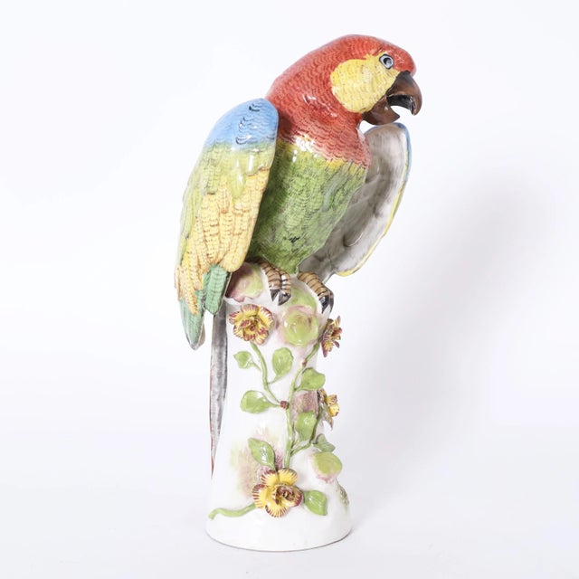 Lofty life size porcelain parrot hand decorated in vivid tropical colors, glazed and perched on a tree trunk. Signed with...