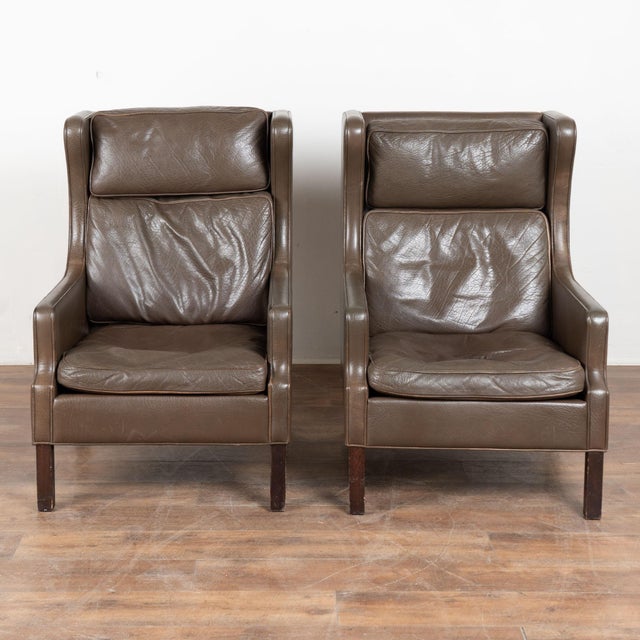 Pair of mid century Danish club chairs upholstered in chocolate brown vintage leather. Mid century modern in style, the...