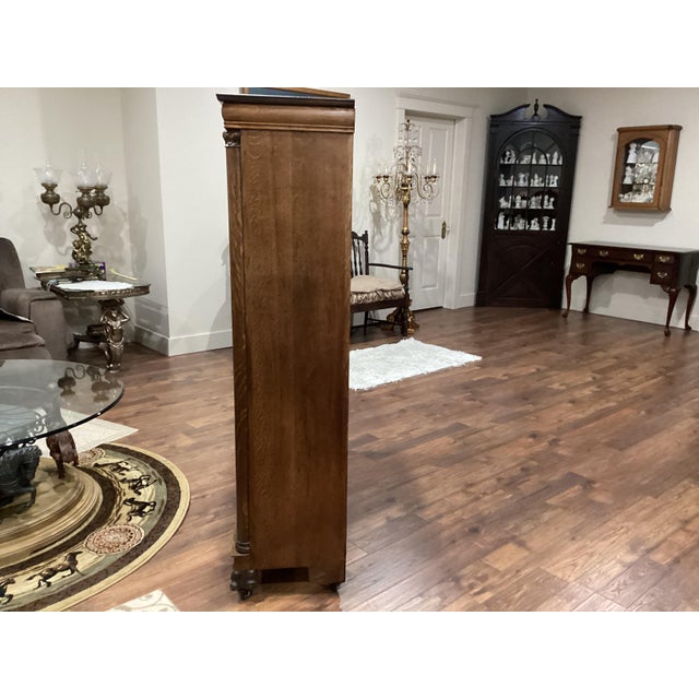 This antique oak bookcase features double doors with leaded glass panels adorned with tulips, standing on carved feet that...