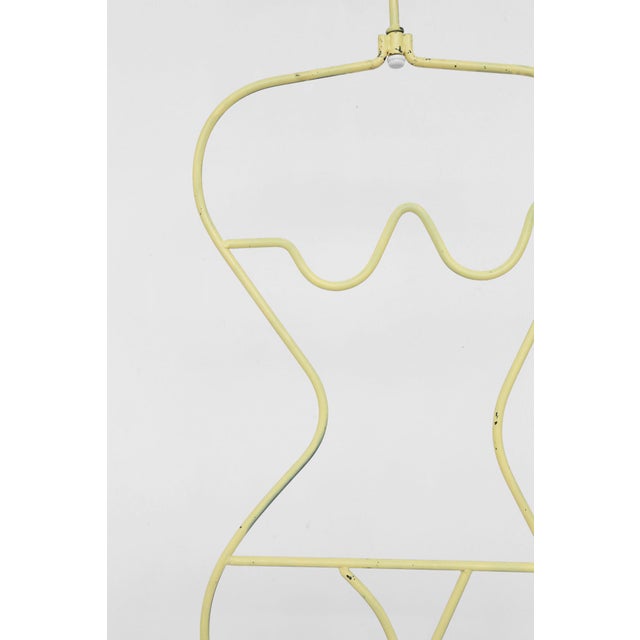 Pale yellow painted steel mannequin with sculptural, feminine form. A wooden sphere at the top provides a perch for hats...