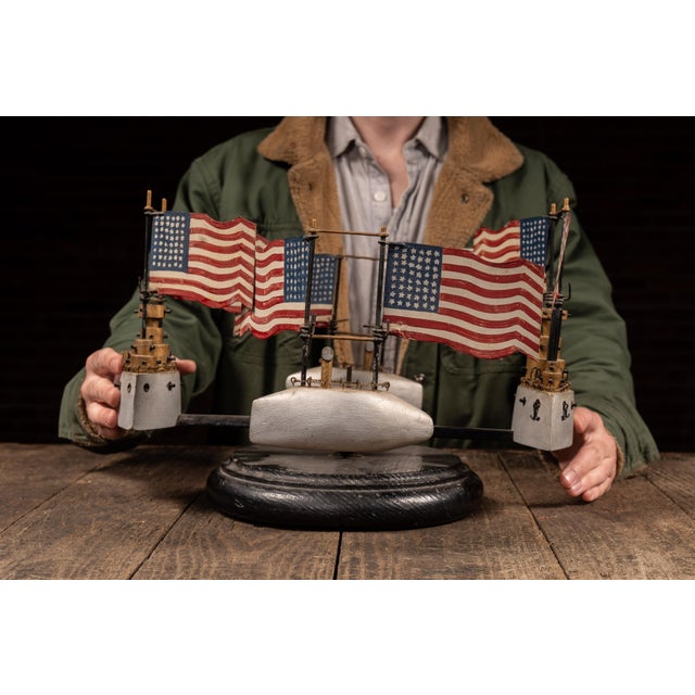 Handcrafted folk art whirligig featuring a circular arrangement of painted American flags mounted on wire supports,...
