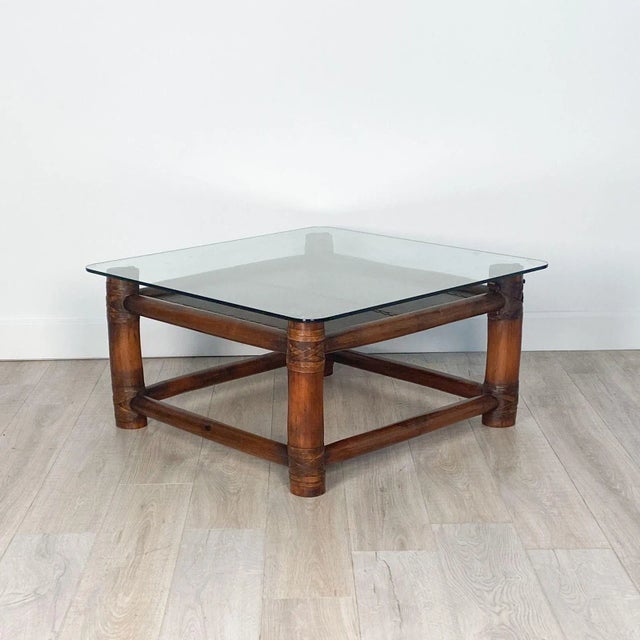 A Vintage McGuire Style coffee table with a glass top and a shelf covered in leather.