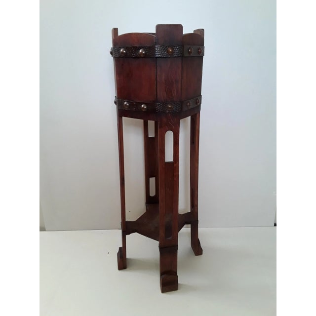 This is a square flower stand in oak wood, wrought iron and studded with strict Art Nouveau ornaments.