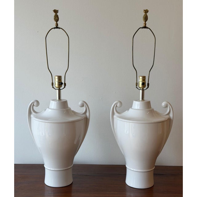 A pair of vintage ceramic table lamps in a classic urn form, finished in a smooth white glaze. Each features gently curved...