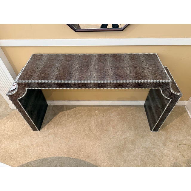 Wrapped in rich, hornback crocodile‑embossed leather and edged with gleaming nickel nailheads, this console table delivers...