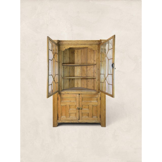 A beautiful antique English pine corner cabinet dating to circa 1880, featuring a warm natural pine finish, glazed upper...