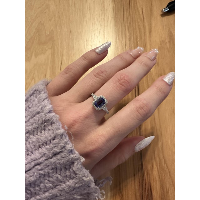 A tanzanite rests in a deep violet-blue at the heart of this solid 14K white gold ring, flanked by thirty-eight earth-...