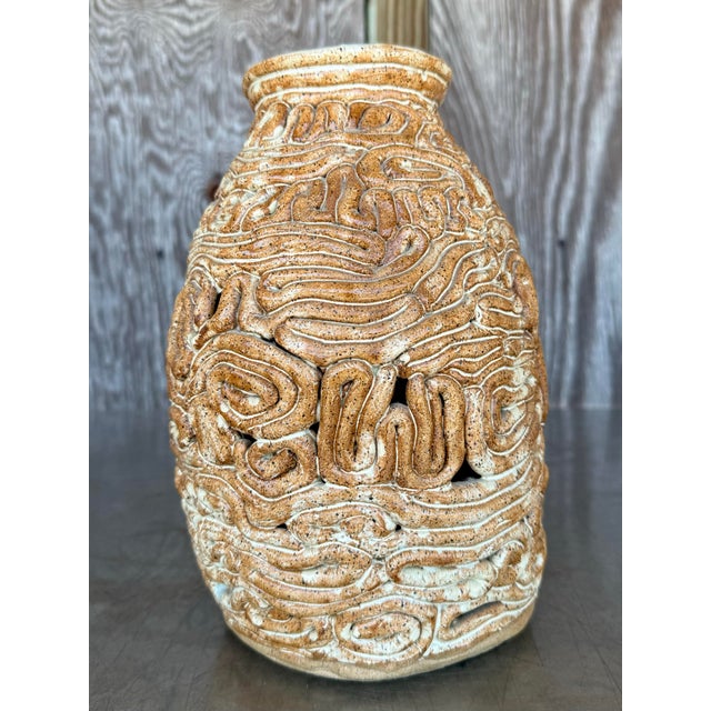 his ceramic coil pot features a hand-built construction with visible spiral forms wrapping rhythmically around its center,...