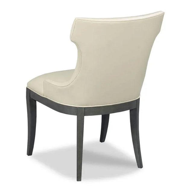 A curved upholstered back wraps around an upholstered seat with welt trim raised by graceful tapering saber legs.