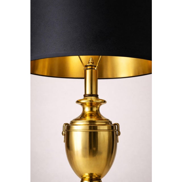 Vintage Hollywood Regency polished brass urn table lamp with original black shade featuring a gold-lined interior. Elegant...