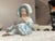 Vintage bisque porcelain figurine depicting a young girl wearing a soft blue bonnet and coordinating dress. This charming...