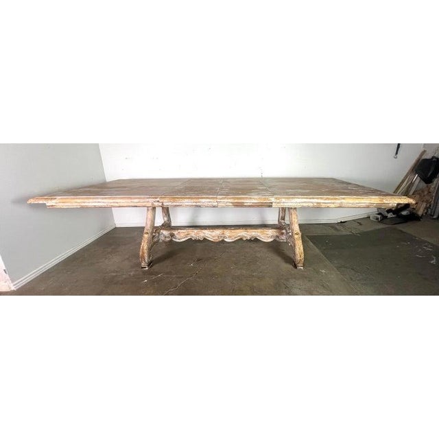 Italian carved wood painted trestle dining table with leaves. The table has a vintage, weathered look. It is made of wood...