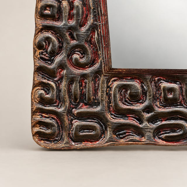 A striking decorative wall mirror with an intricately hand-carved wood frame featuring abstract, Oceanic-inspired motifs....