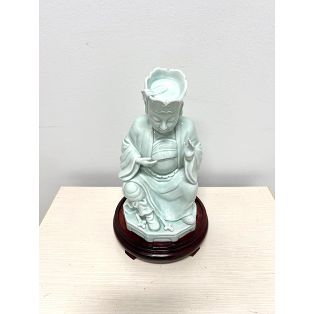 An Asian style Buddha figurine with wood stand by Andrea by Sadek. Hand painted, light blue color glazed porcelain of a...