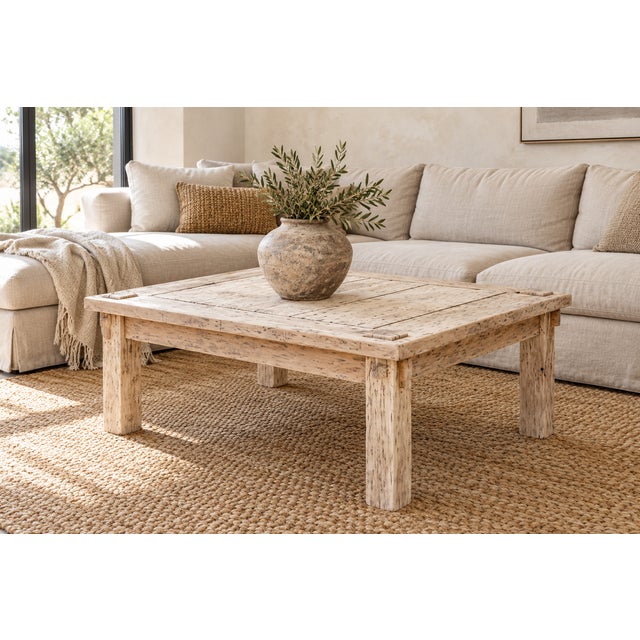 A coffee table with a plank top in bleached teak, the surface worn to a soft gray-white with the dark grain still showing...