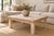 A coffee table with a plank top in bleached teak, the surface worn to a soft gray-white with the dark grain still showing...