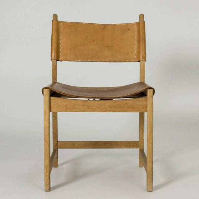 Elegant chair by Kurt Østervig, with a boxy oak silhouette and leather seat and back. Details of white seams on the...