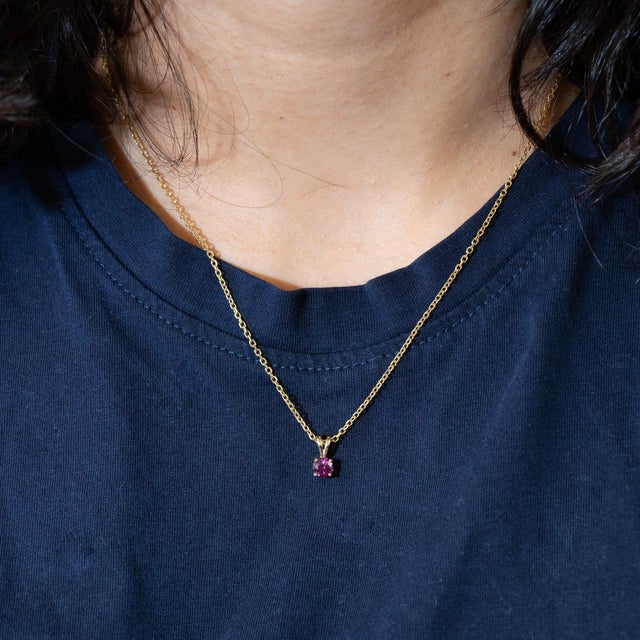 A 0.61-carat red rhodolite garnet round set in solid 14K yellow gold as a classic solitaire pendant. Rhodolite is garnet...