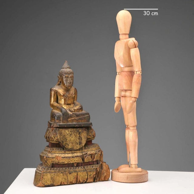 A carved, lacquered, and gilded wooden Buddha figure. Seated on a lotus-shaped base. This piece is attributed to the...