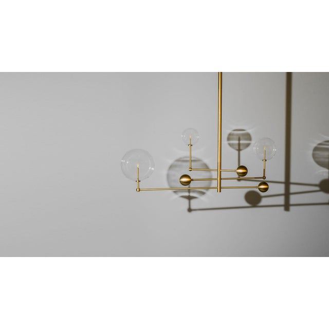 Three illuminated glass globes orbit a central gravitational axis. Rotating brass arms evoke the mechanical grace of the...