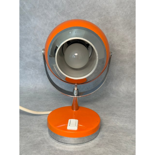 Striking 1970s Space Age eyeball desk lamp featuring a spherical lamp head in a vibrant orange color. Chrome and aluminum...